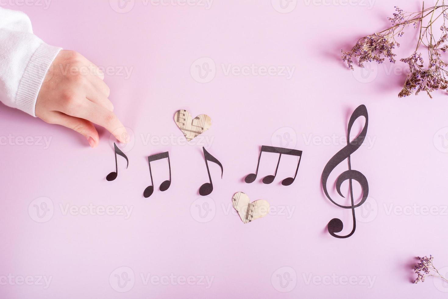 Paper musical clef, paper notes and children's hand on pink. Music education. Top view. photo