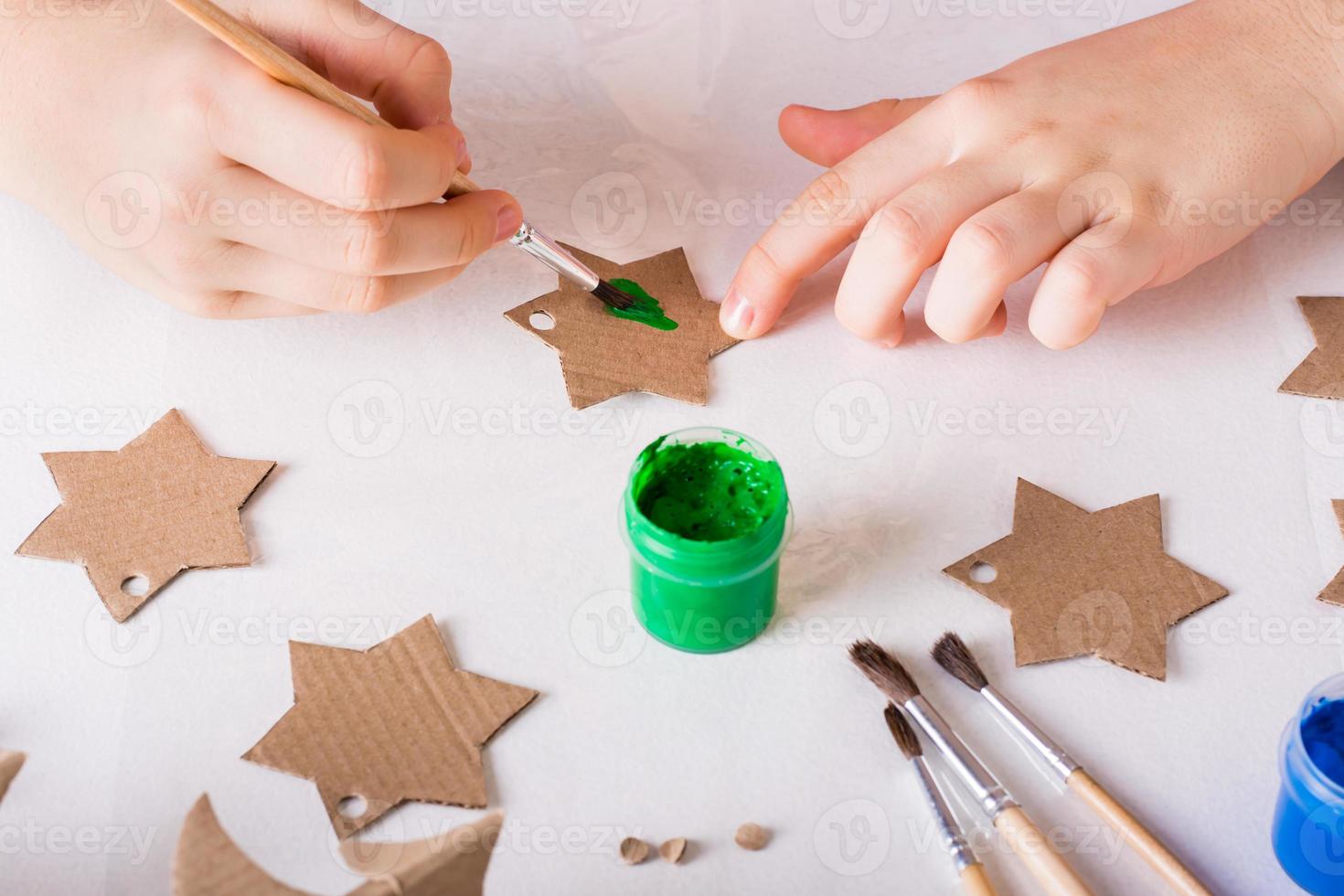 las manos de los niños pintan una estrella de cartón para decoraciones navideñas hechas a mano. foto