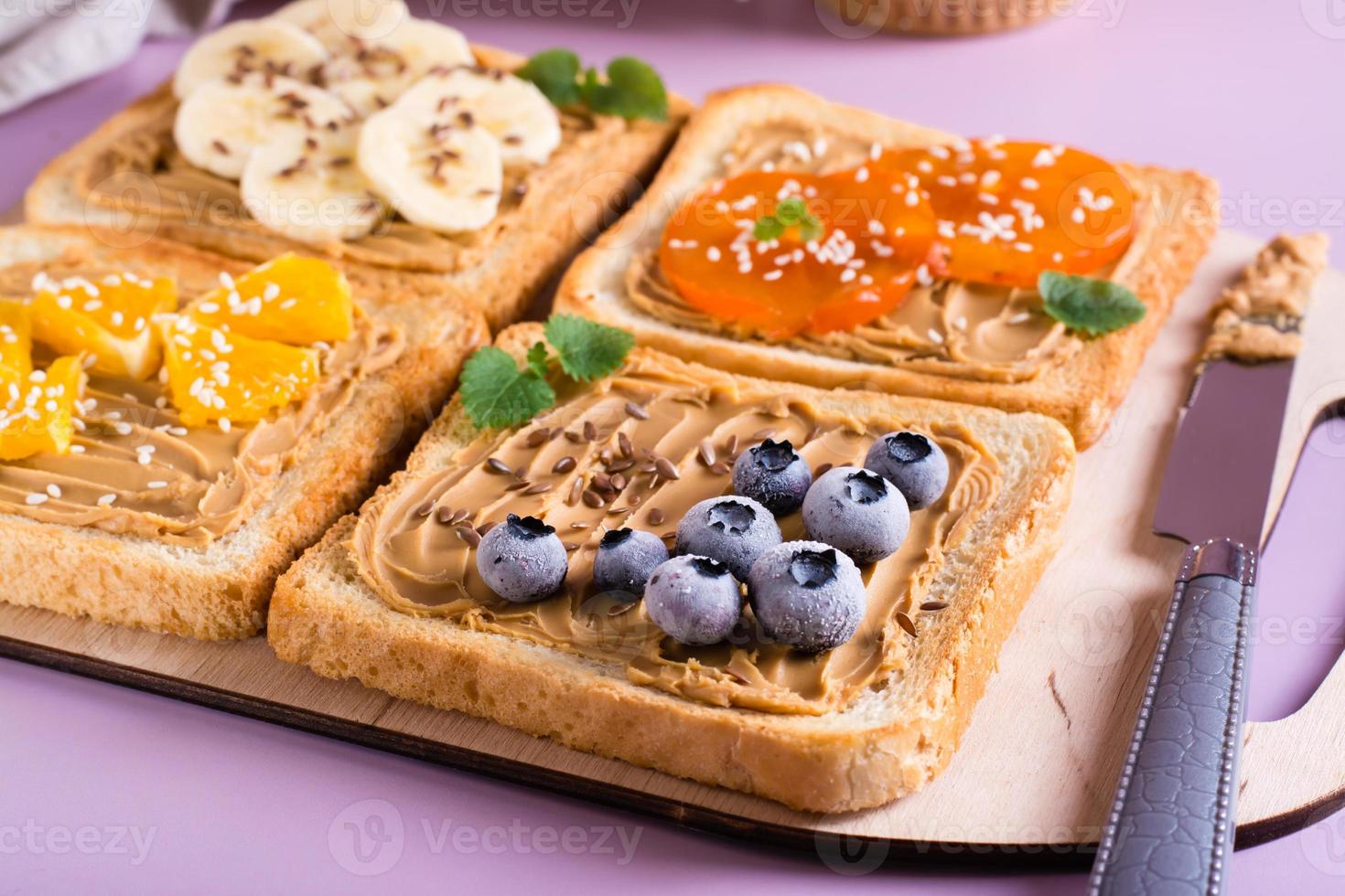 Toast with peanut butter, fruits, berries, flax seeds and sesame seeds on a cutting board. photo