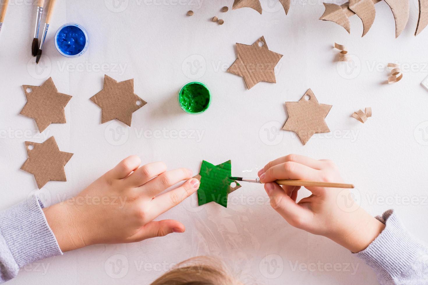 las manos de los niños pintan una estrella de cartón para decoraciones navideñas hechas a mano. vista superior. foto