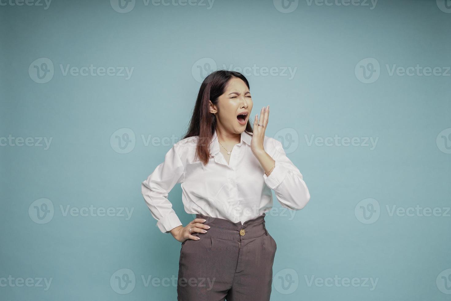 retrato de una mujer asiática soñolienta y atractiva con una camisa blanca, sintiéndose cansada después de la noche sin dormir, bostezando, cubriendo la boca abierta con la palma foto