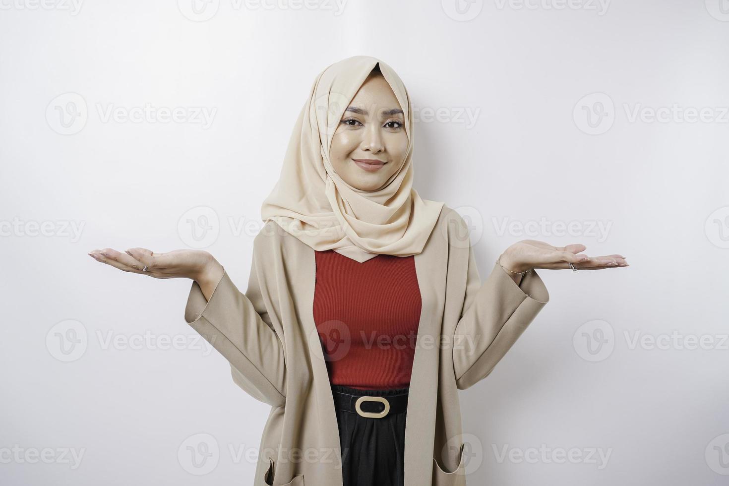 Excited Asian woman wearing hijab pointing at the copy space beside her, isolated by white background photo