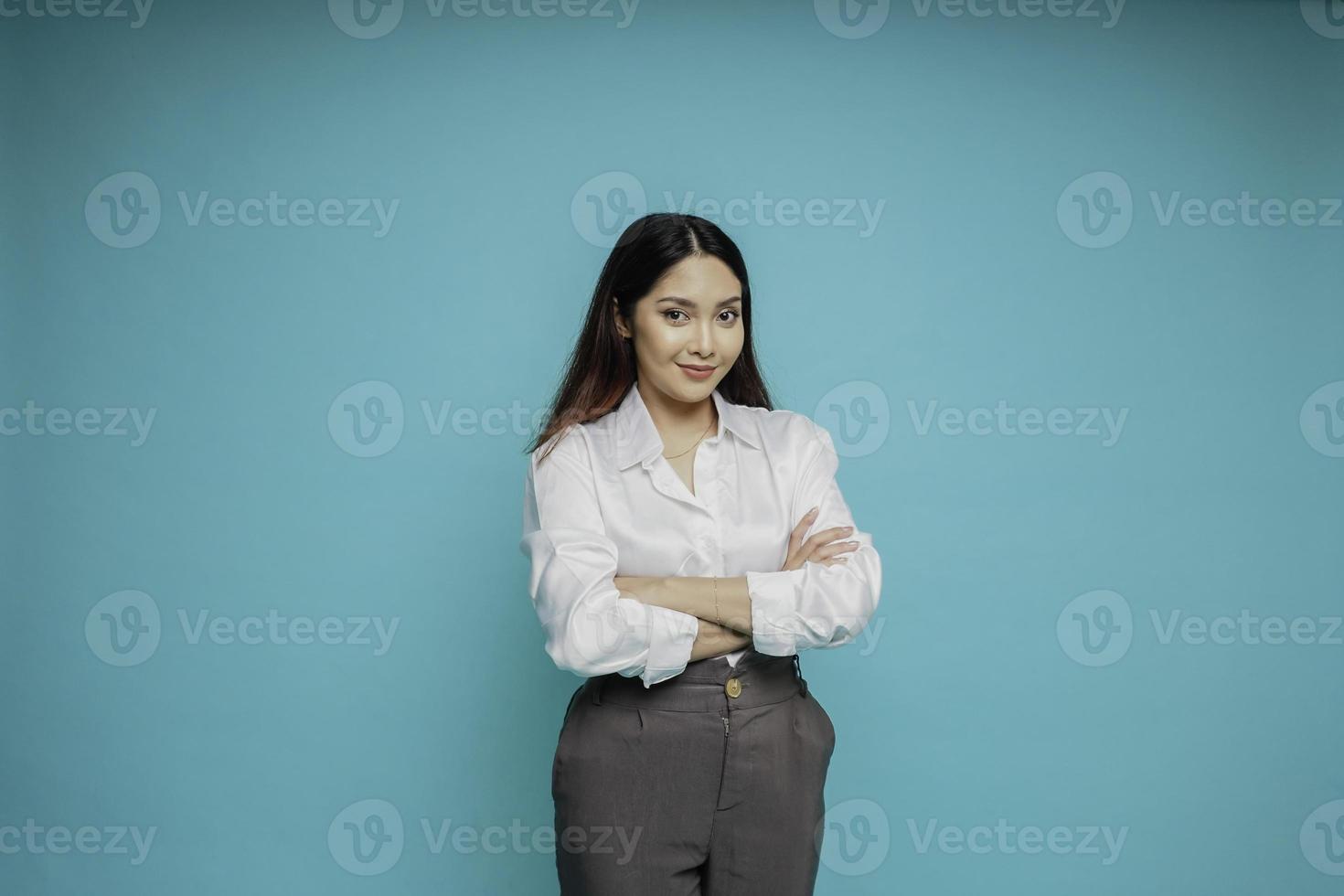 Portrait of a confident smiling Asian woman wearing white shirt standing with arms folded and looking at the camera isolated over blue background photo
