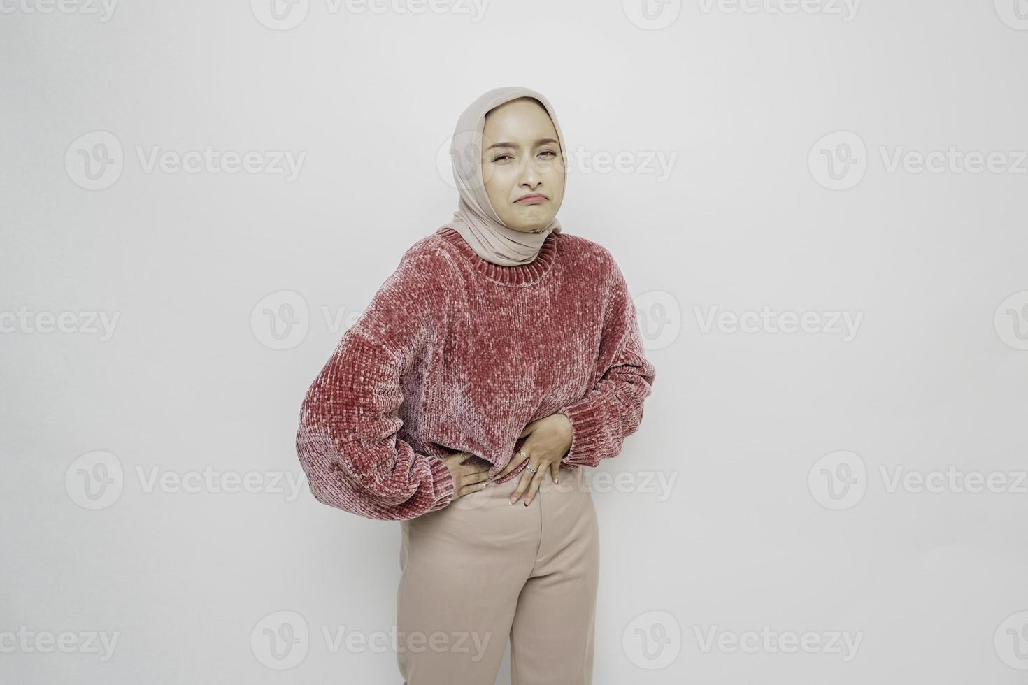 Photo of young unwell sick ill Asian Muslim woman hold hand on stomach suffers pain isolated on white background