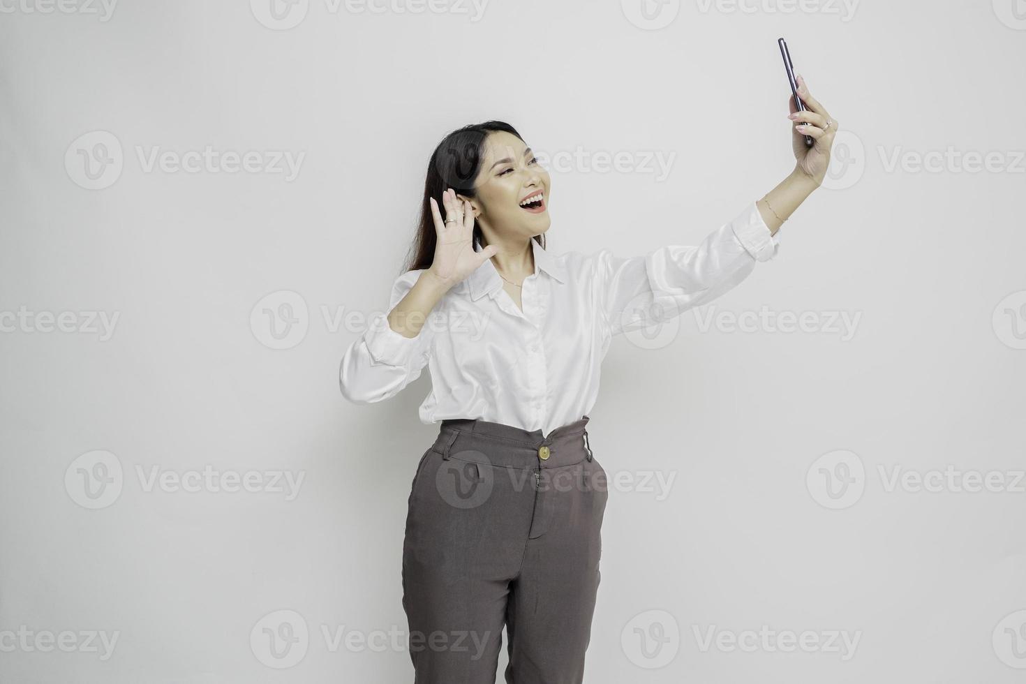 un retrato de una mujer asiática feliz con una camisa blanca y sosteniendo su teléfono, aislada por un fondo blanco foto