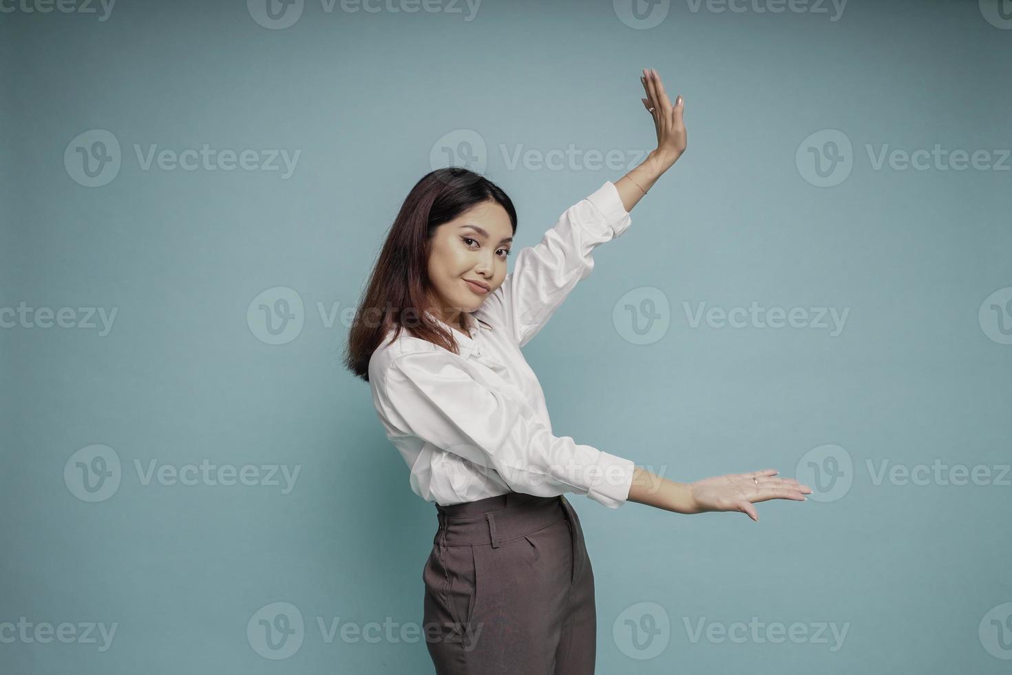 mujer asiática emocionada con pantalones blanco apuntando al espacio de copia a su lado, aislada por fondo azul foto