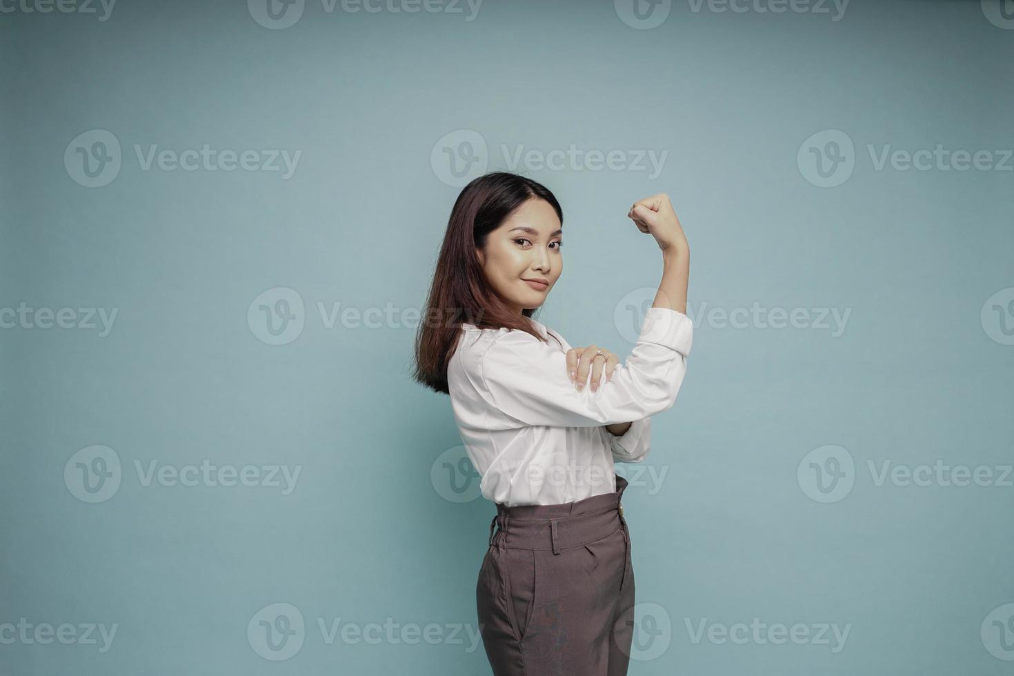 mujer asiática emocionada con una camisa blanca que muestra un gesto fuerte levantando los brazos y los músculos sonriendo con orgullo foto