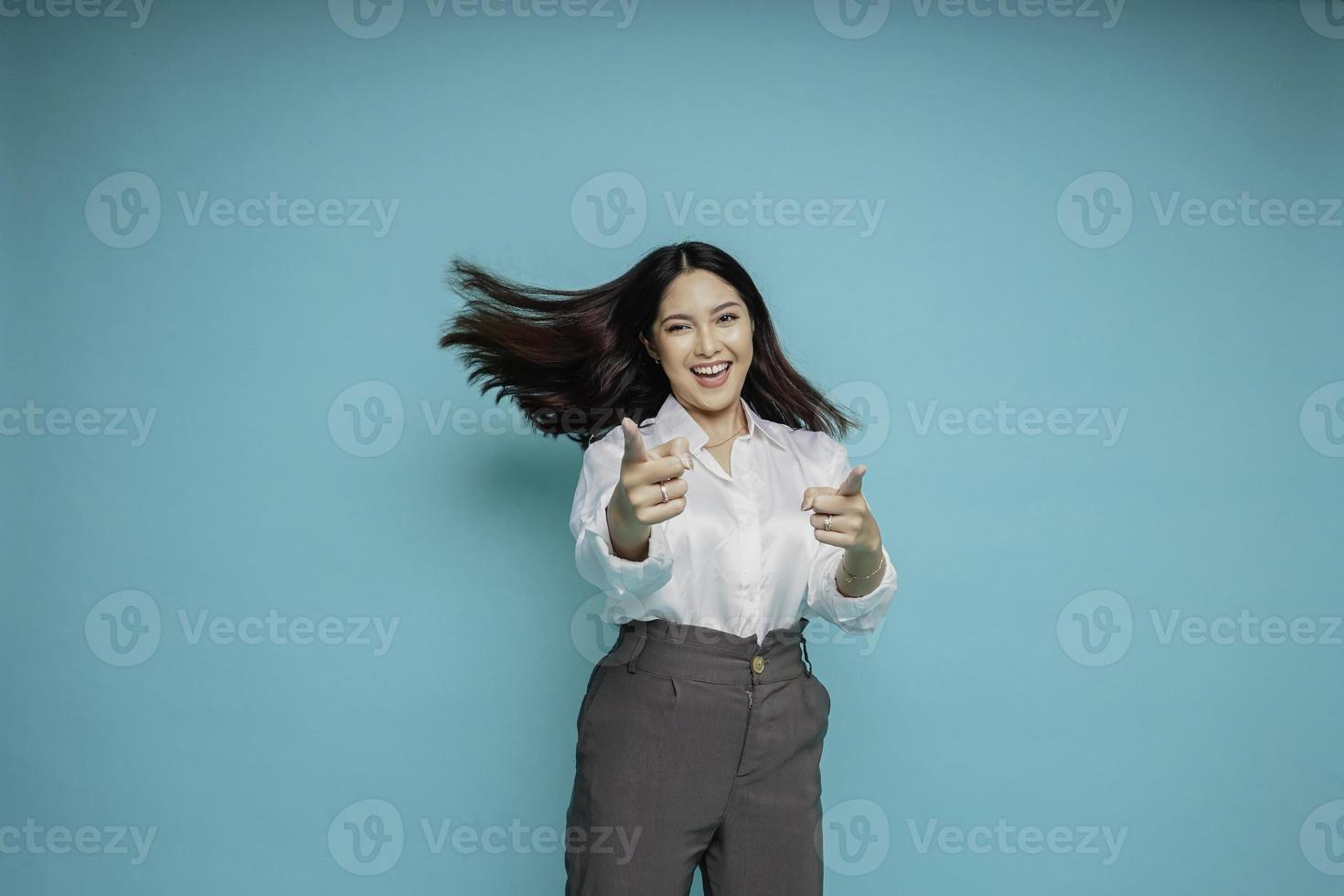 Excited Asian woman wearing white shirt pointing at the camera, isolated by blue background photo