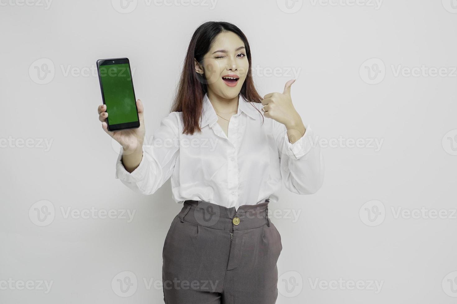 Excited Asian woman wearing white shirt gives thumbs up hand gesture of approval while showing copy space on her phone photo