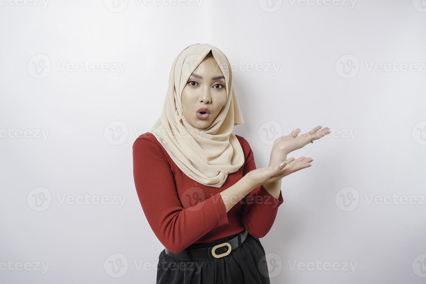 Shocked Asian woman wearing hijab pointing at the copy space beside her, isolated by white background photo