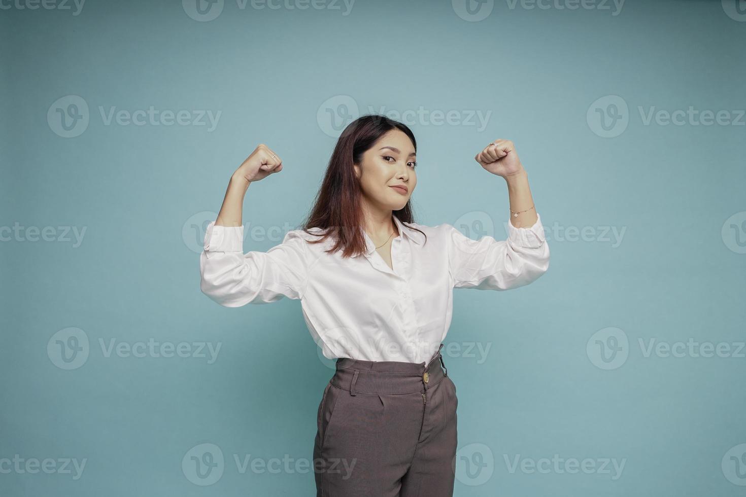 Excited Asian woman wearing a white shirt showing strong gesture by lifting her arms and muscles smiling proudly photo