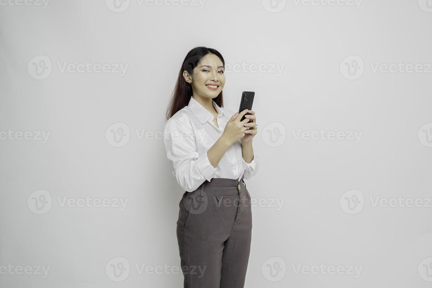 A portrait of a happy Asian woman wearing a white shirt and holding her phone, isolated by white background photo