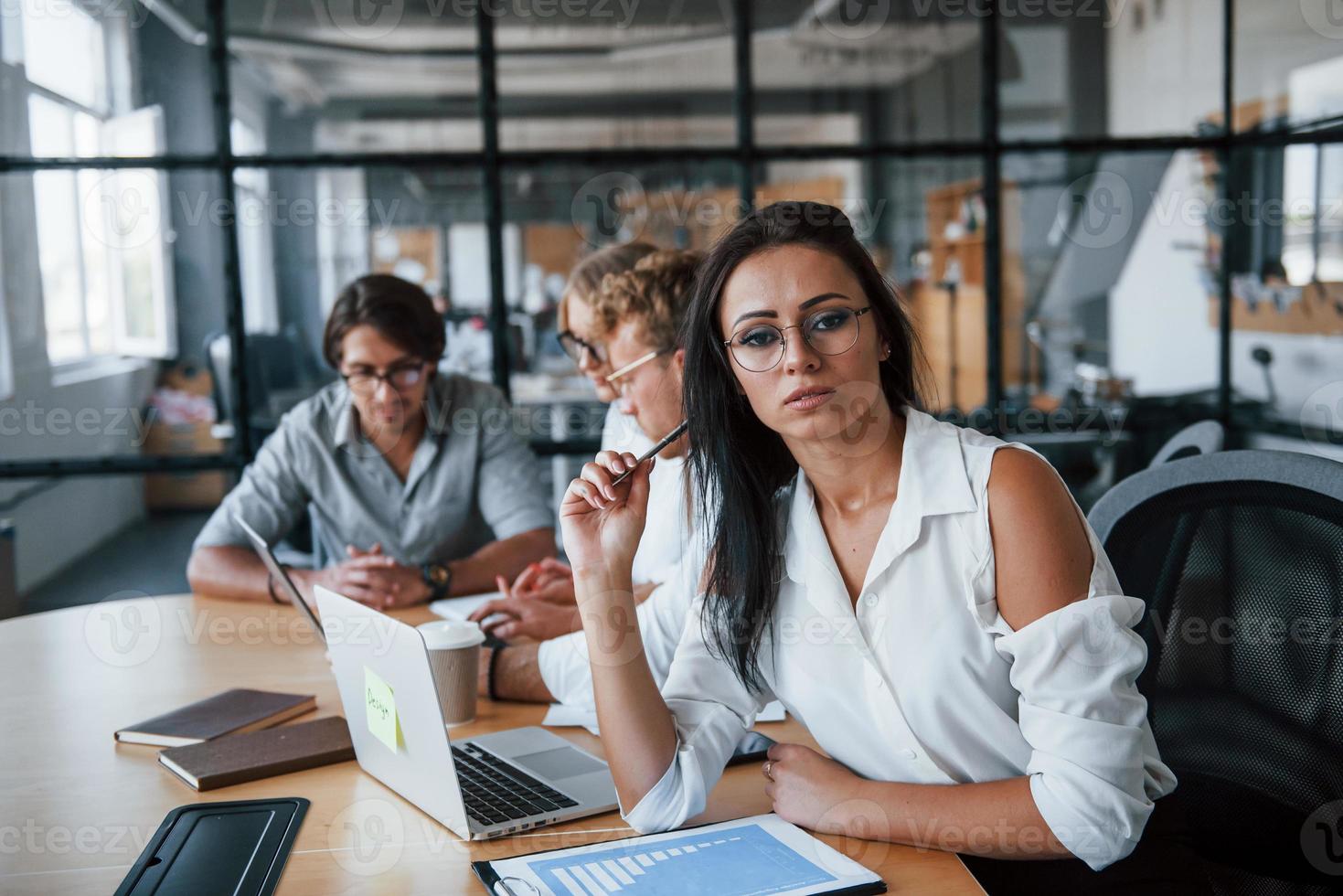 mujer morena frente a los empleados. jóvenes empresarios vestidos de forma formal trabajando en la oficina foto