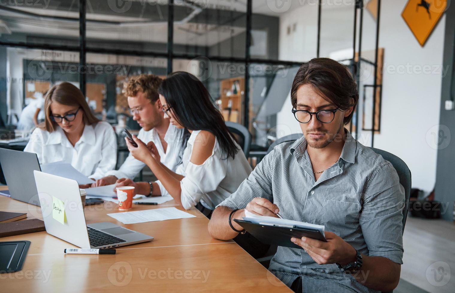 Guy in glasses in front of his employees. Young business people in formal clothes working in the office photo