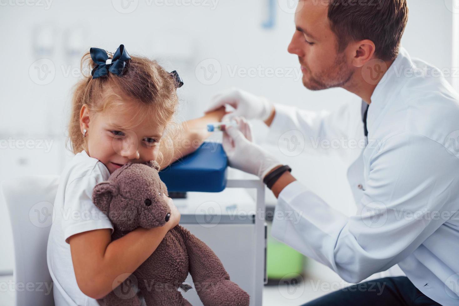 muestra de sangre. niña con su osito de peluche está en la clínica con el médico foto