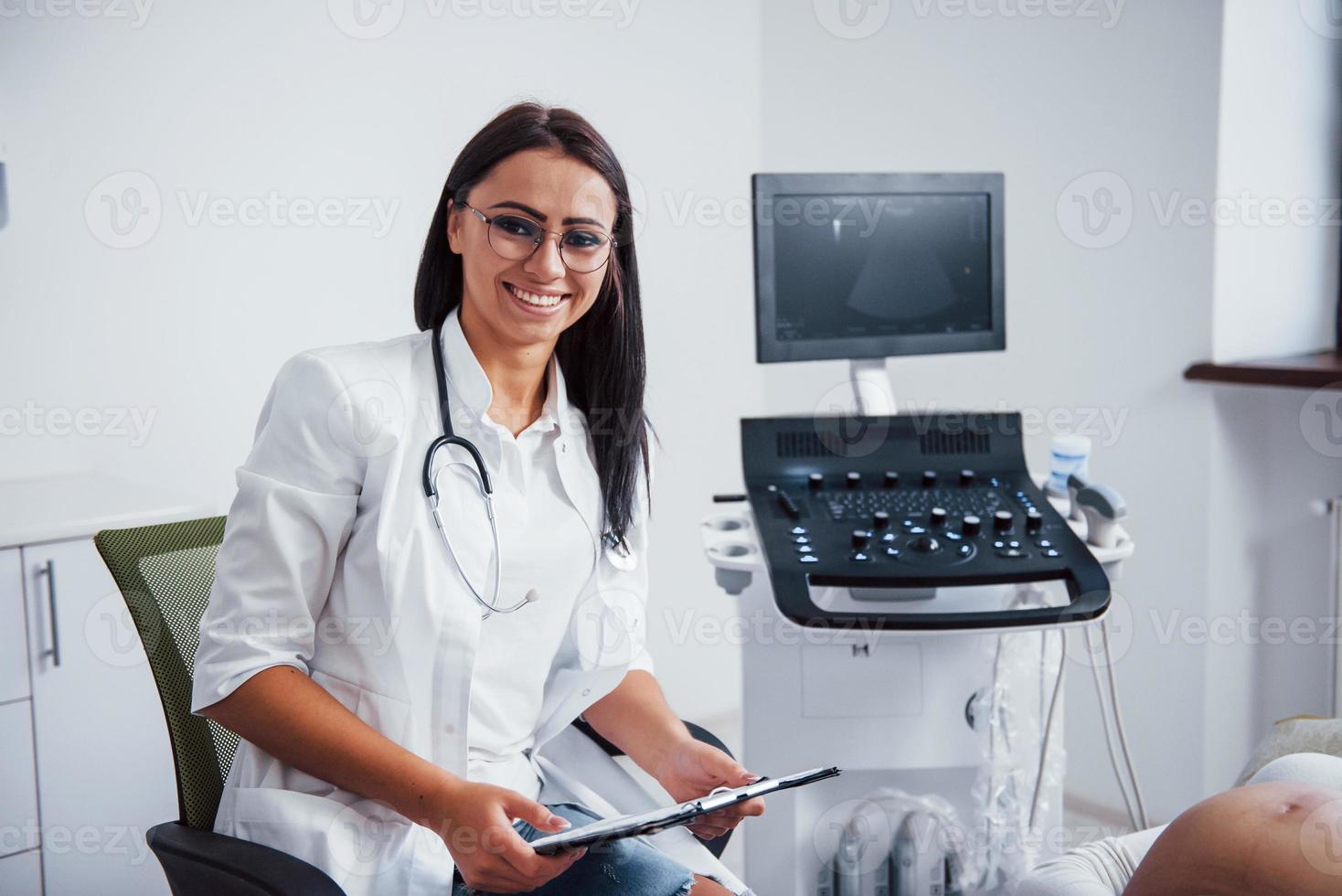 retrato de un médico obstetra que se sienta en la sala de la clínica con un dispositivo de ultrasonido foto