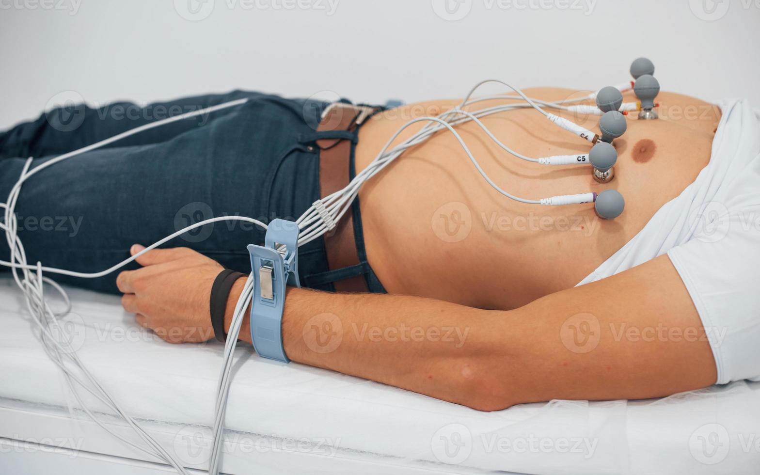 Man lying on the bed in the clinic and getting electrocardiogram test photo