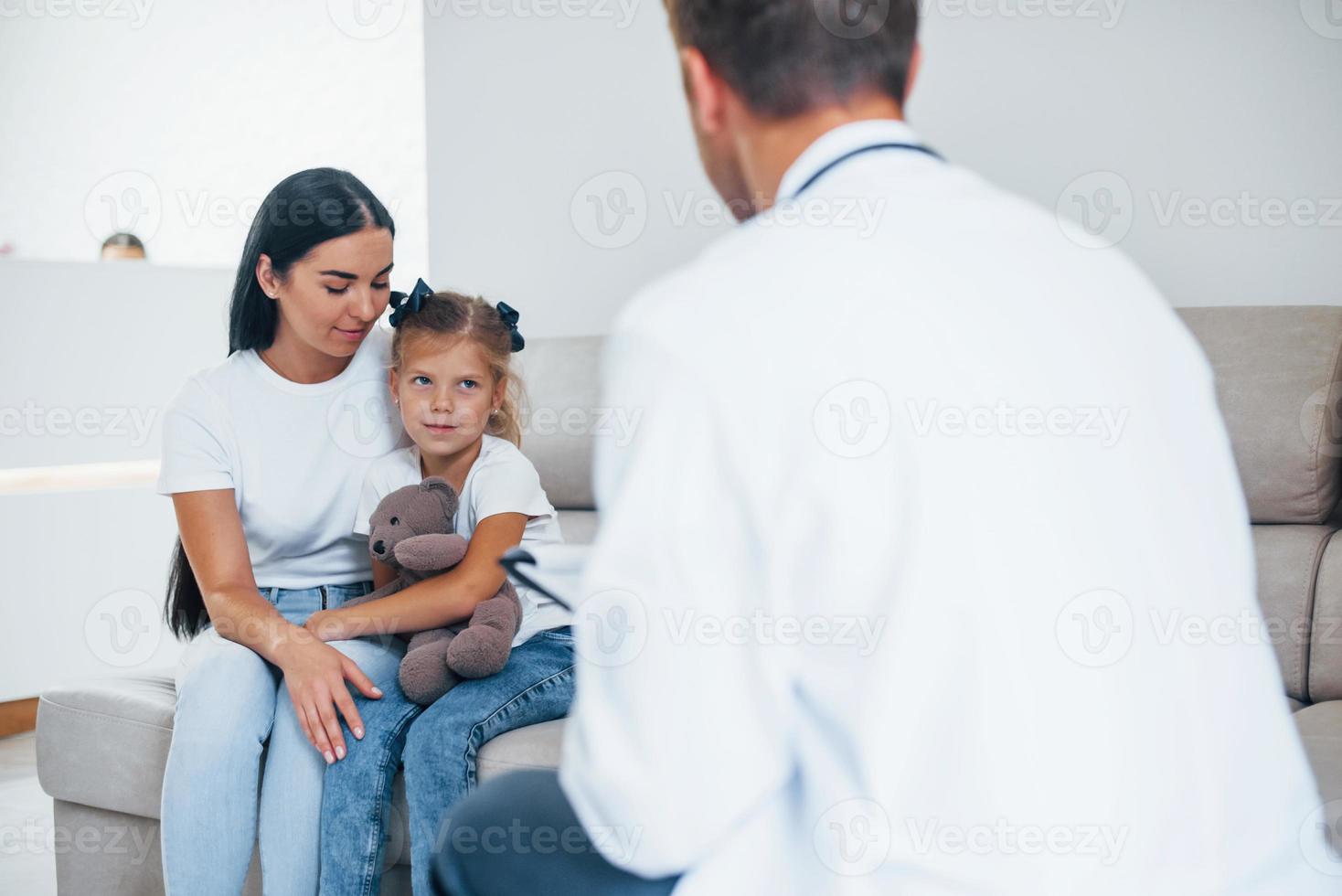 Mother with her cute daughter is visiting clinic. Listening to the doctor photo