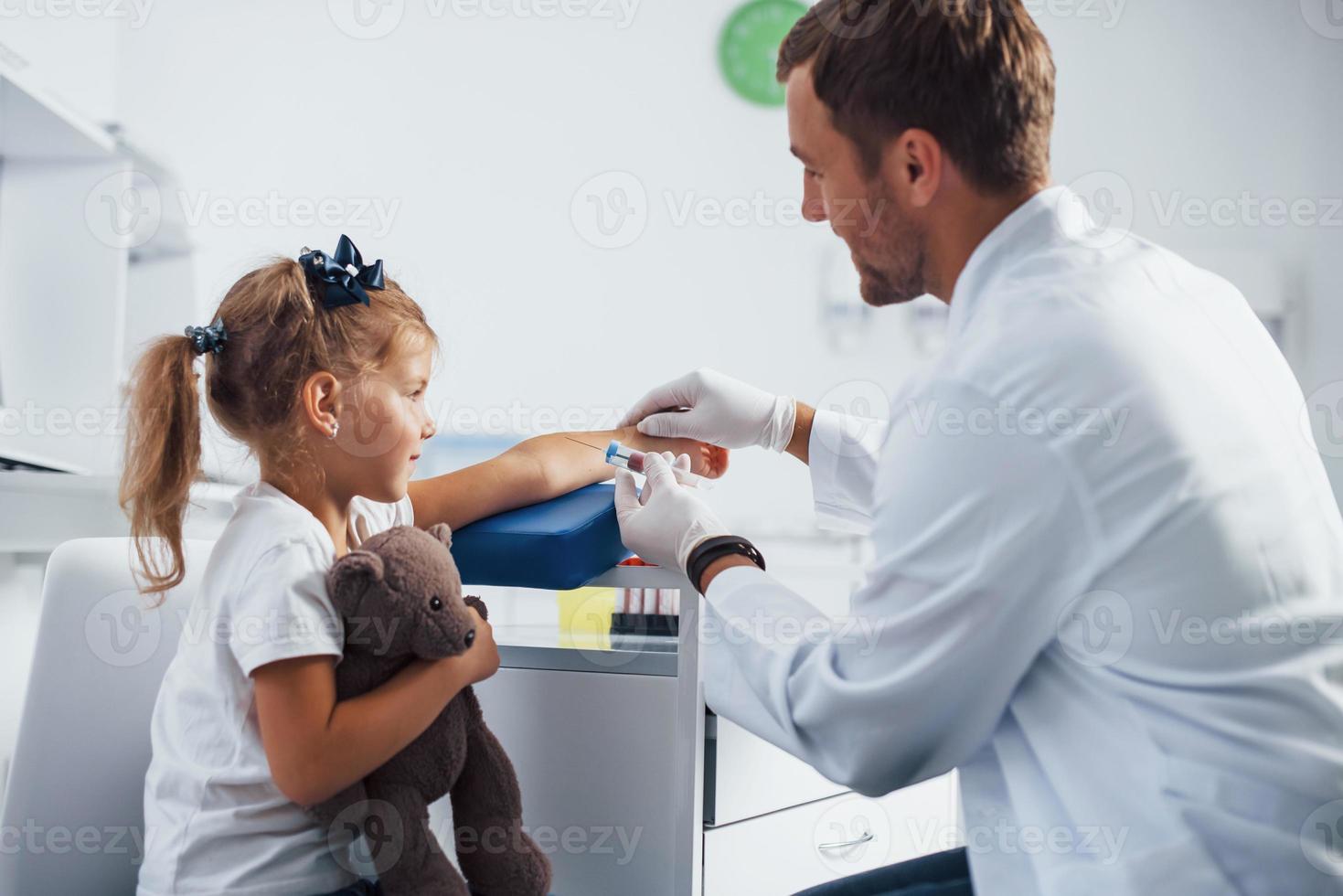 Blood sampling. Little girl with her teddy bear is in the clinic with doctor photo