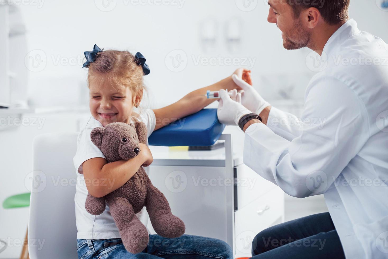 muestra de sangre. niña con su osito de peluche está en la clínica con el médico foto