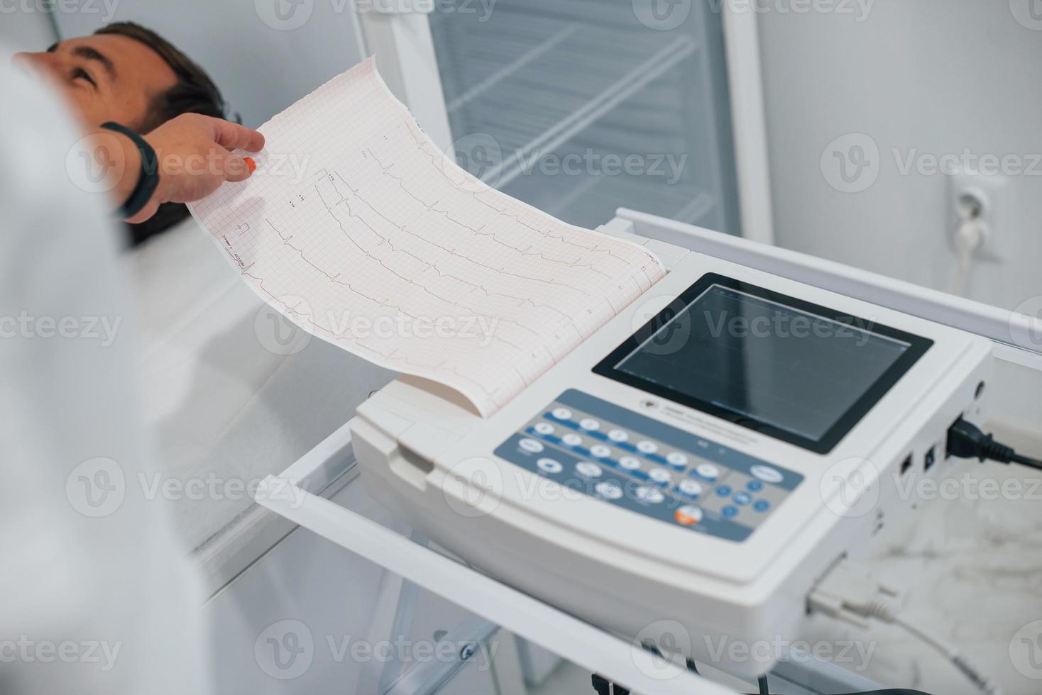 Man lying on the bed in the clinic and getting electrocardiogram test photo