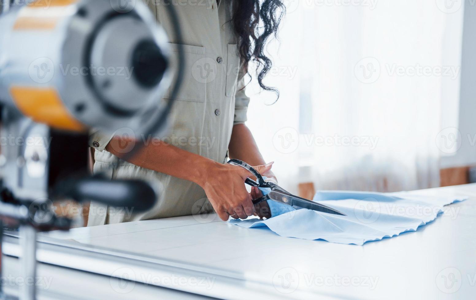 Female worker is in the sewing factory at daytime cutting cloth with scissors photo