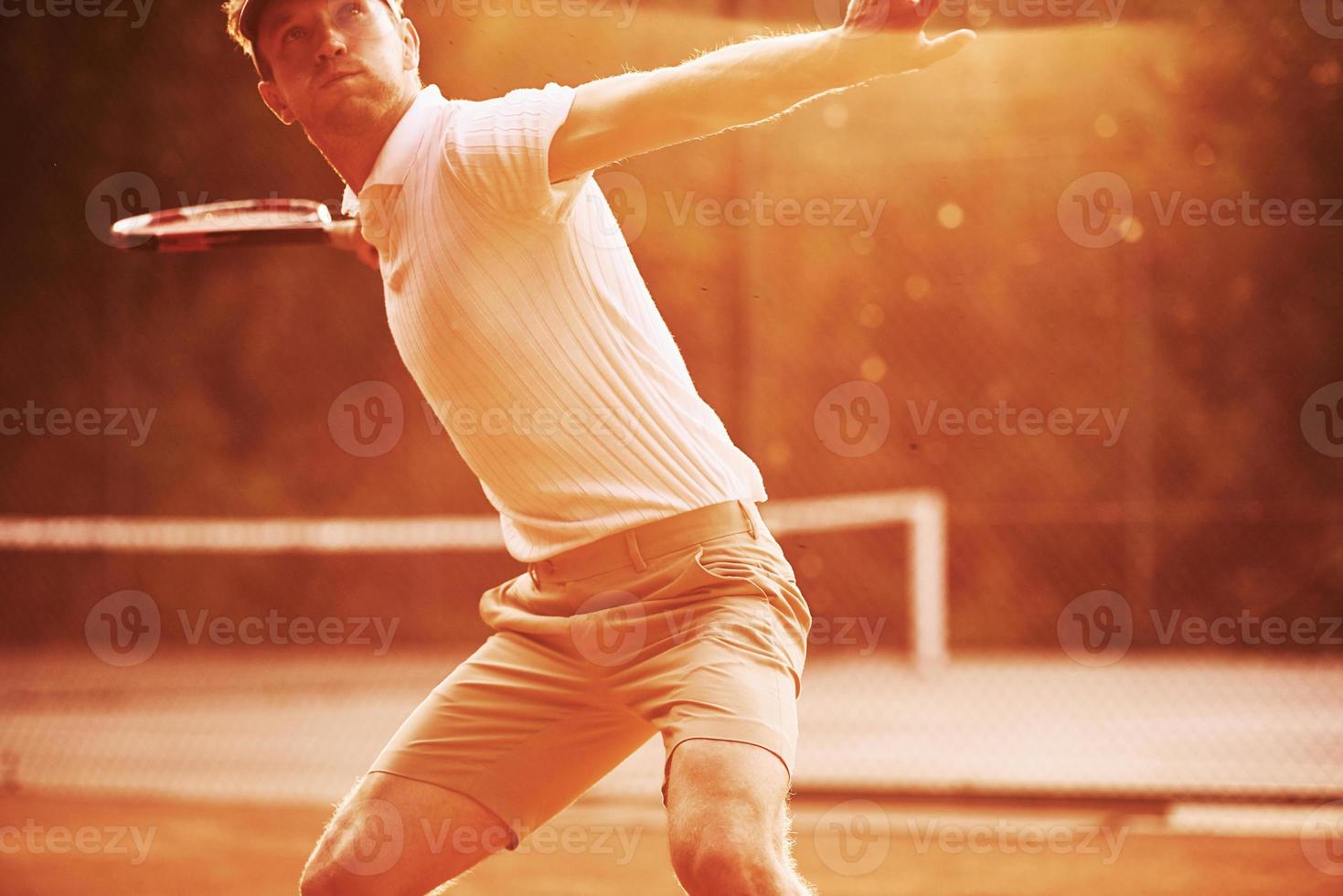 Illuminated by sunlight. Young tennis player in sportive clothes is on the court outdoors photo