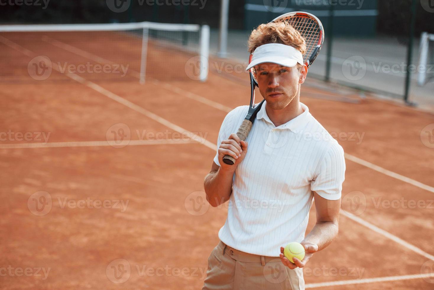 tiene la pelota en la mano. joven tenista con ropa deportiva está en la cancha al aire libre foto