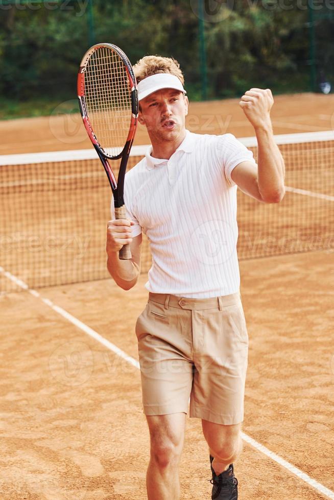 Celebrating victory. Young tennis player in sportive clothes is on the court outdoors photo