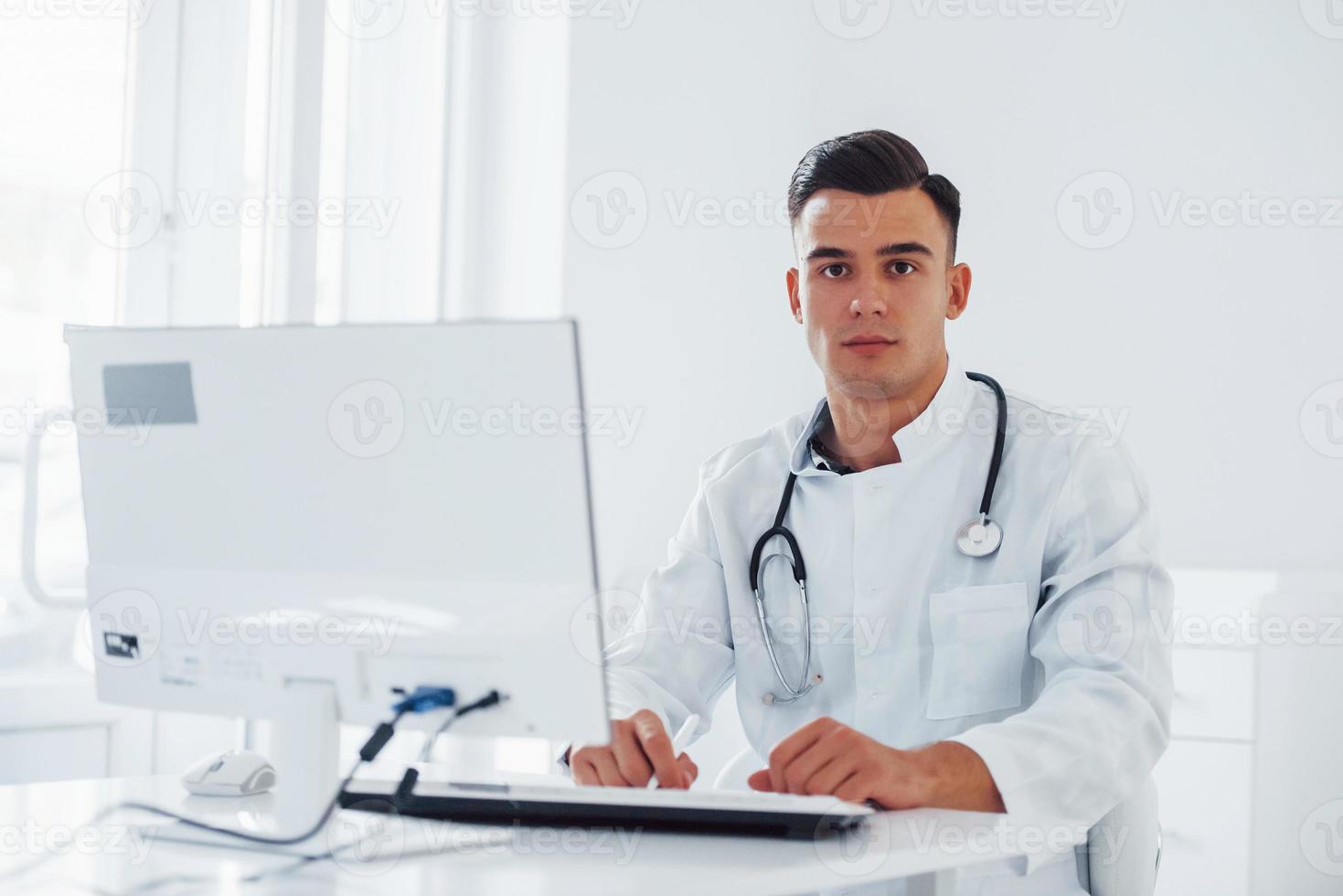 Young stylish male doctor with stethoscope is in clinic at daytime photo