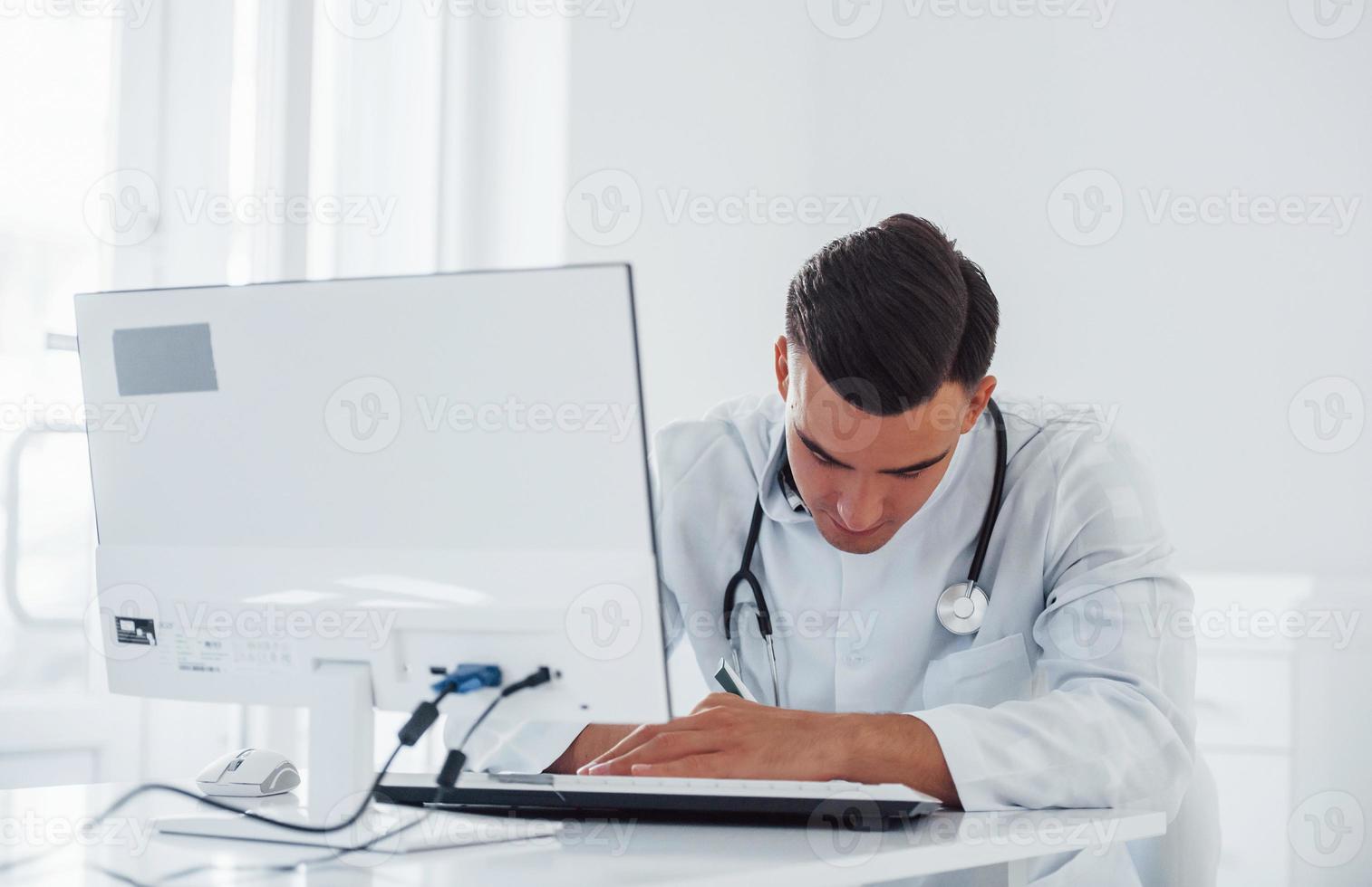 Working with documents. Young stylish male doctor with stethoscope is in clinic at daytime photo