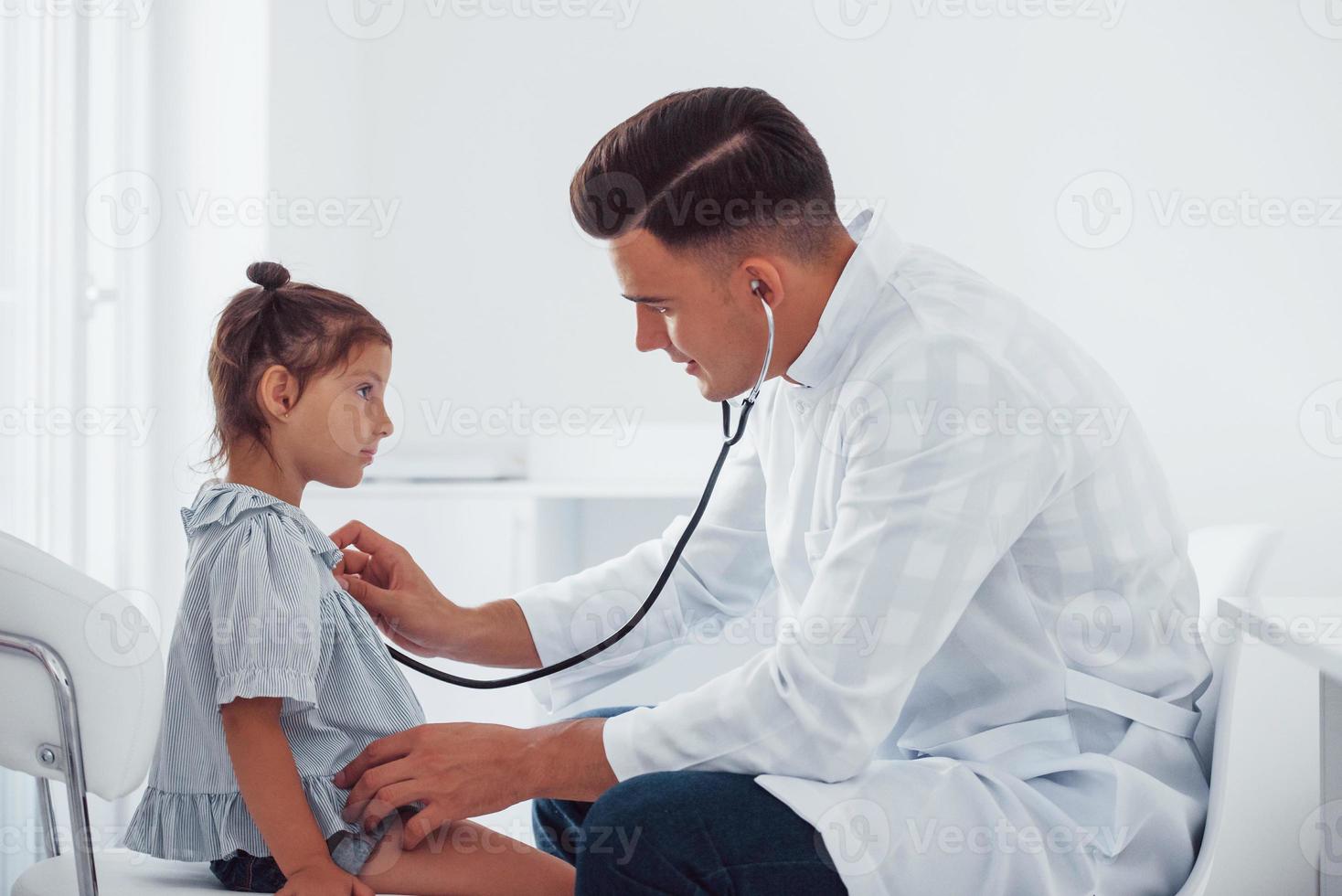 Young pediatrician works with little female visitor in the clinic photo