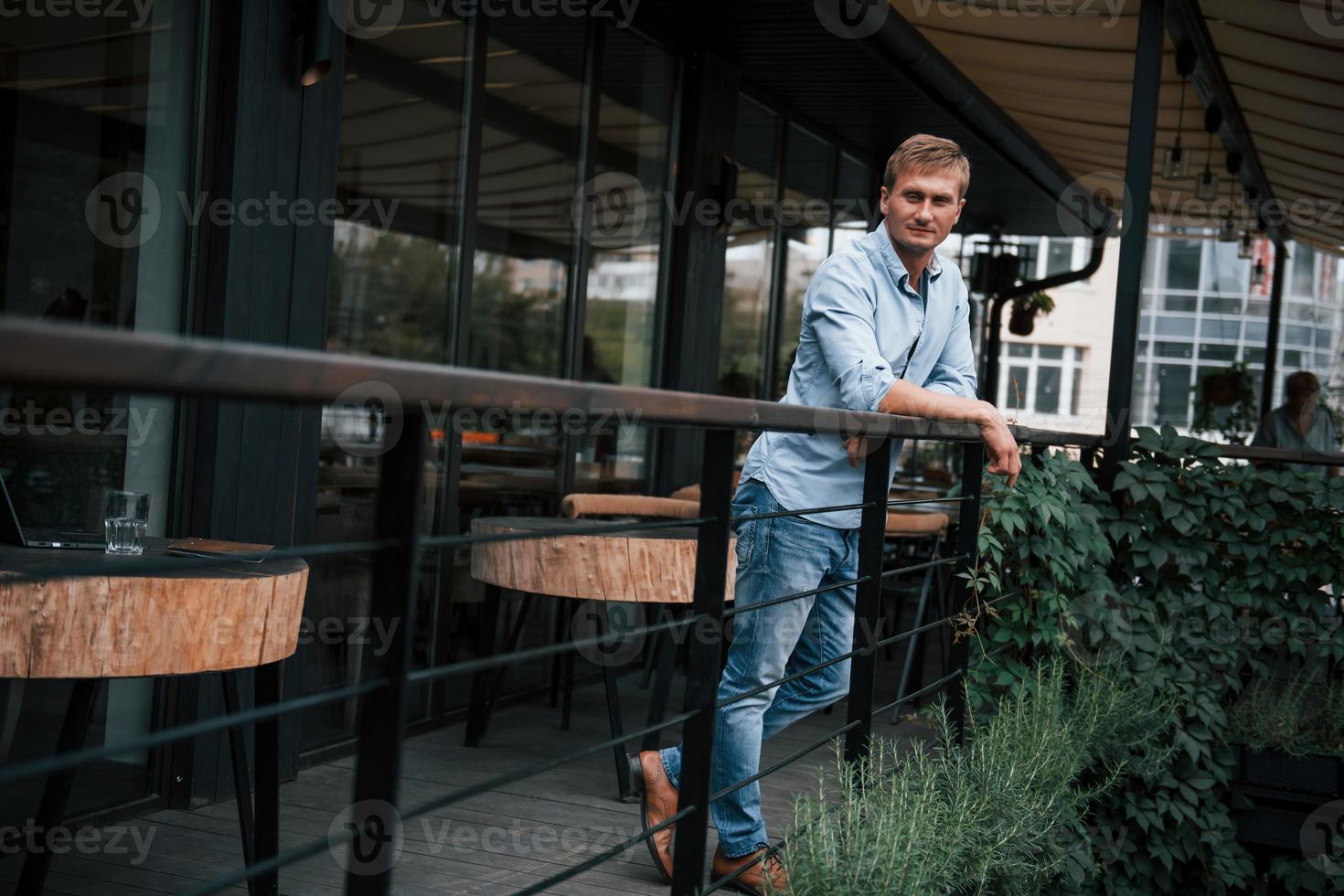 apoyándose en las barandillas. vista frontal del chico en jeans que se para en el café durante el día foto