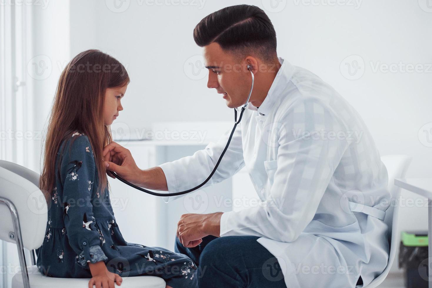 joven pediatra trabaja con una pequeña visitante en la clínica foto