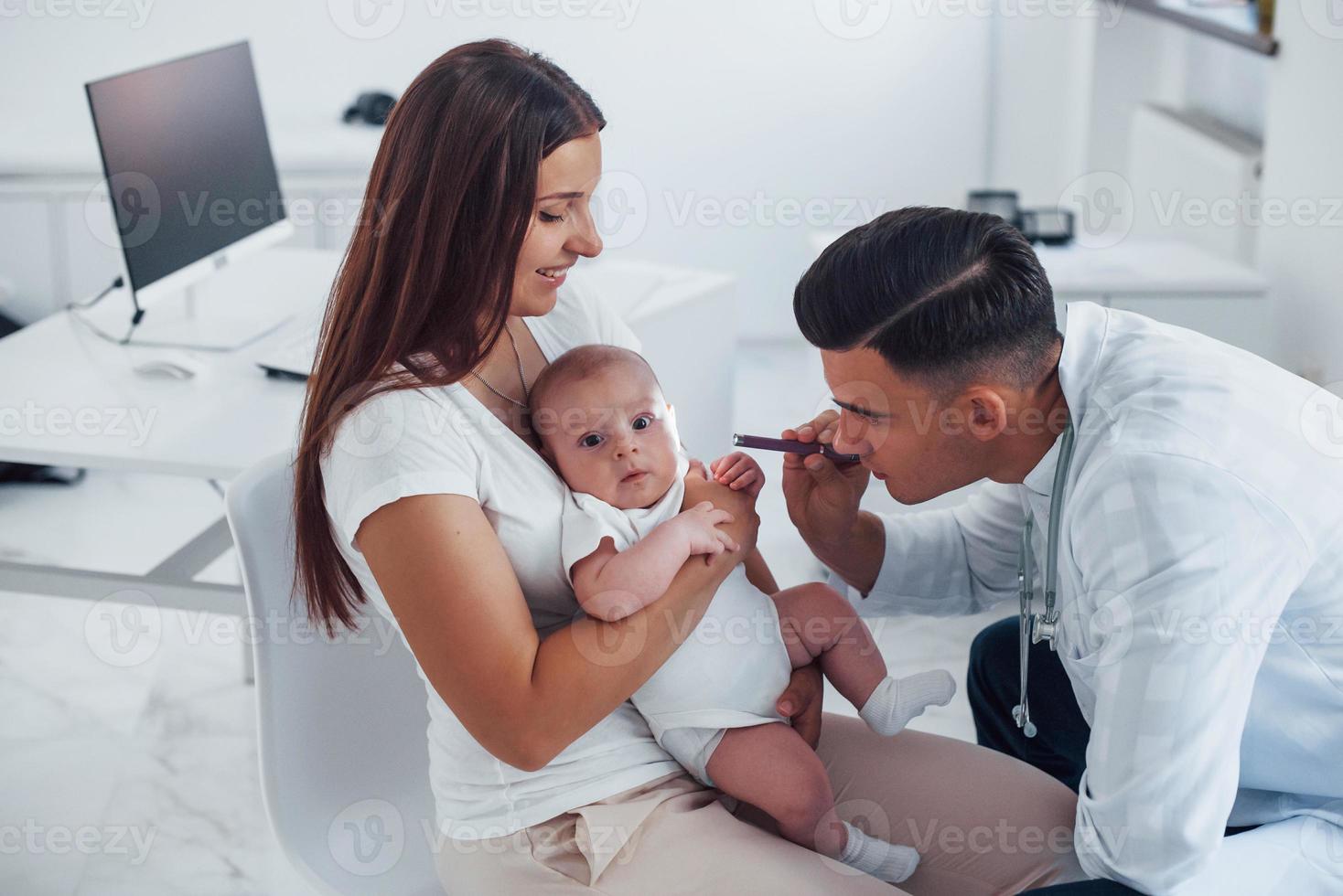 con la ayuda de la madre. el joven pediatra está con un bebé en la clínica durante el día foto