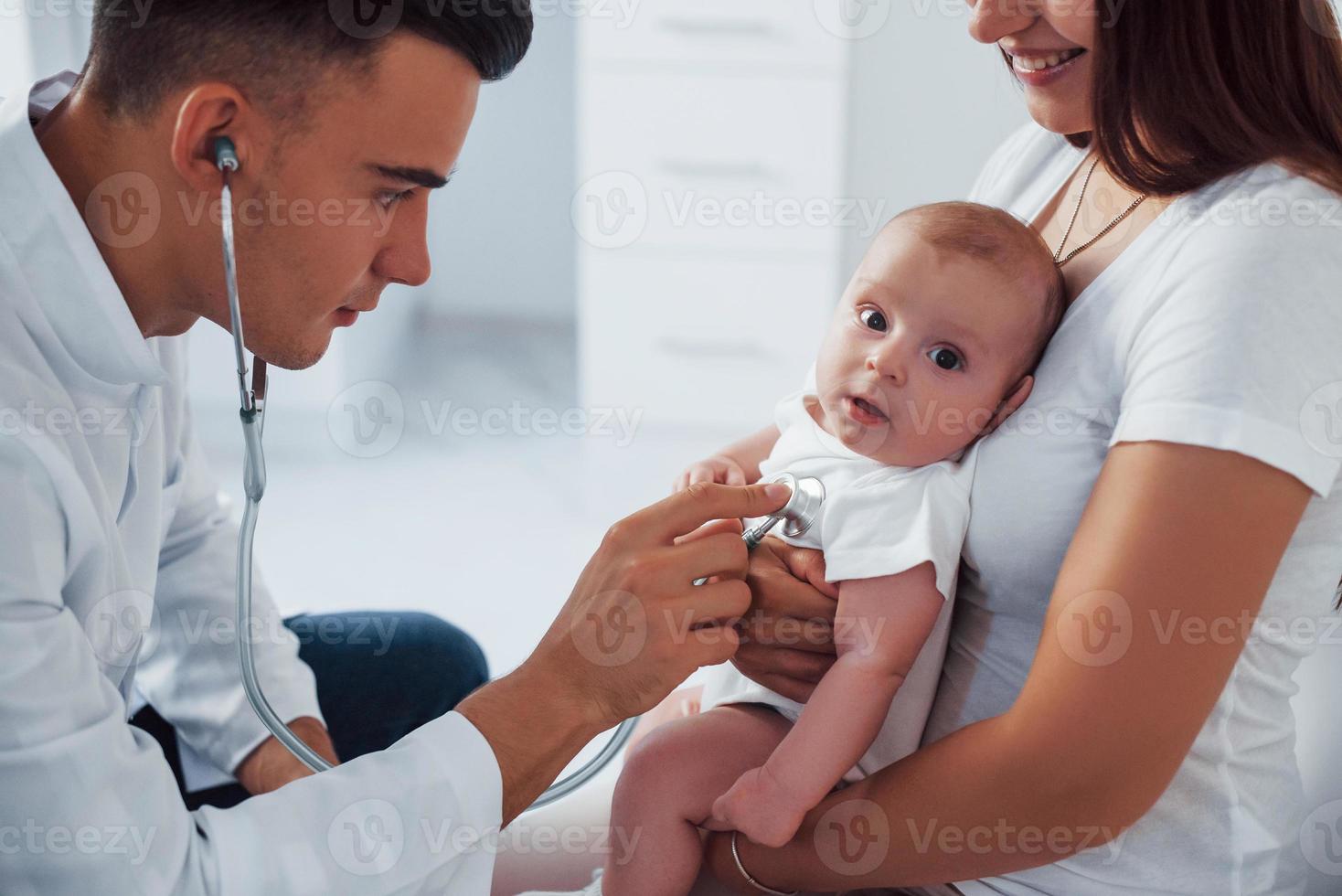 con la ayuda de la madre. el joven pediatra está con un bebé en la clínica durante el día foto