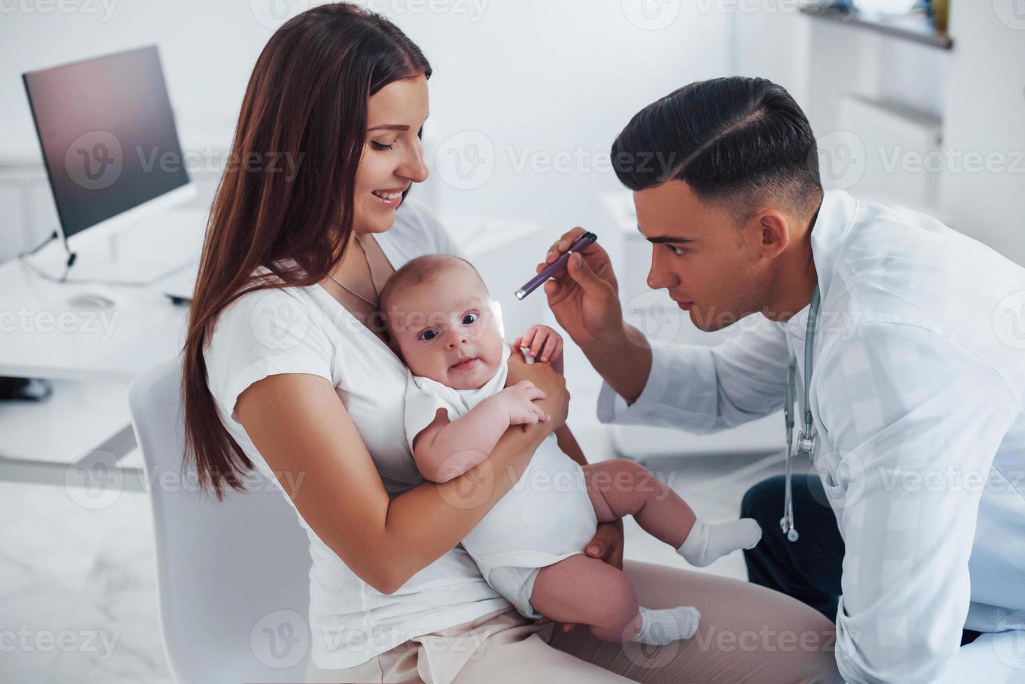 With mother's help. Young pediatrician is with little baby in the clinic at daytime photo