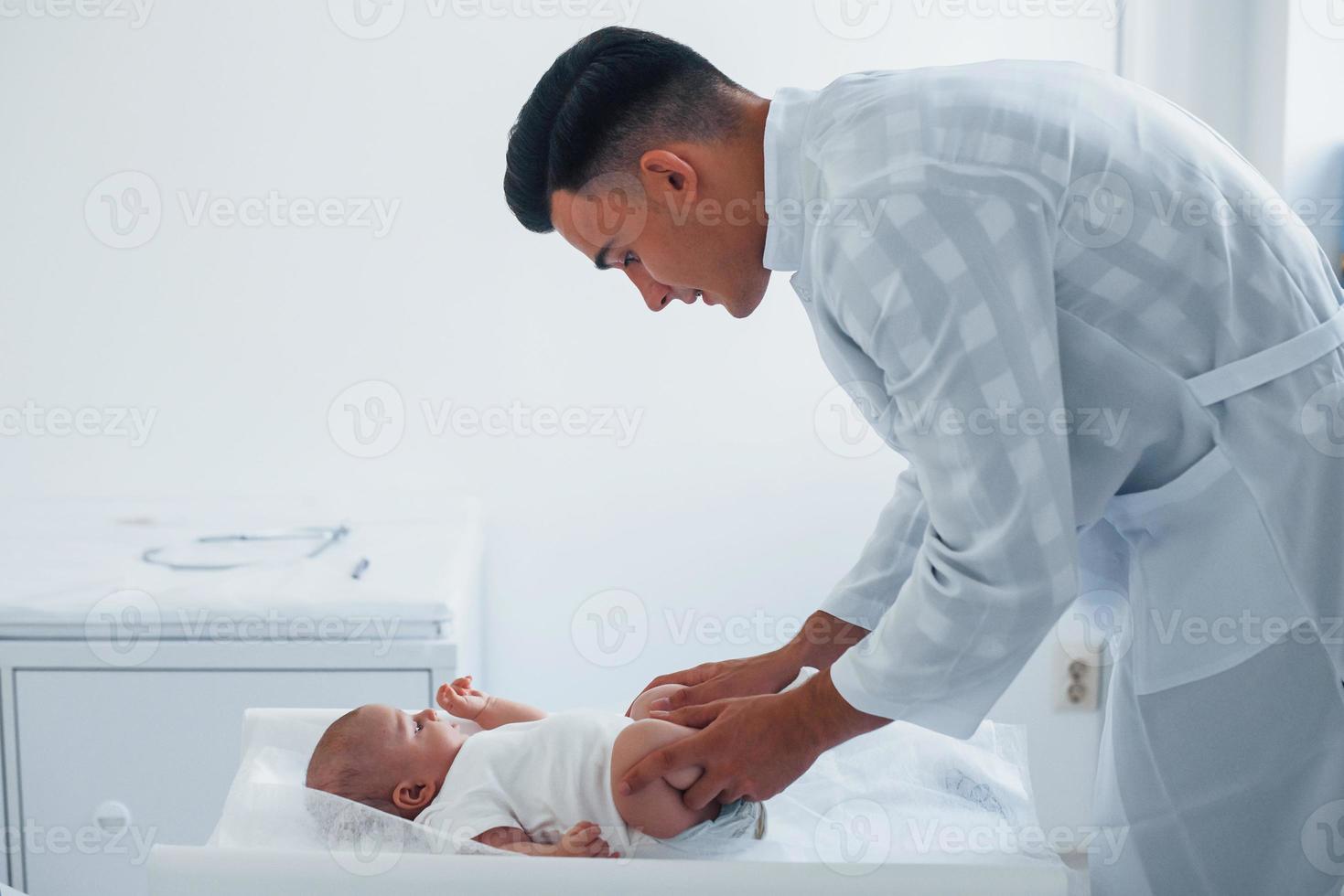 Young pediatrician is with little baby in the clinic at daytime photo