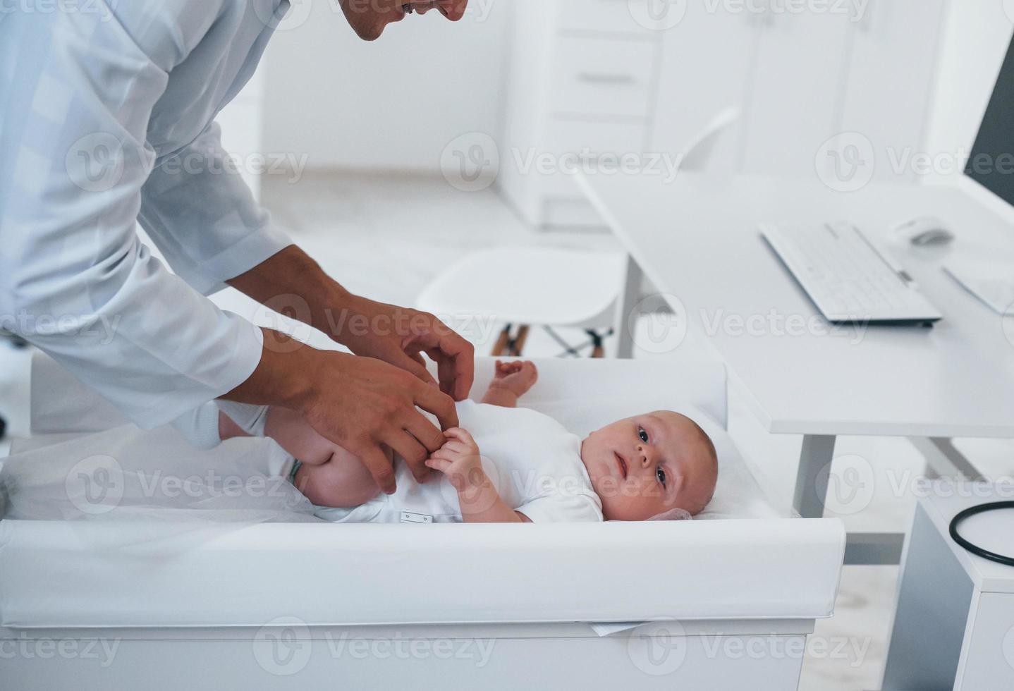 Young pediatrician is with little baby in the clinic at daytime photo