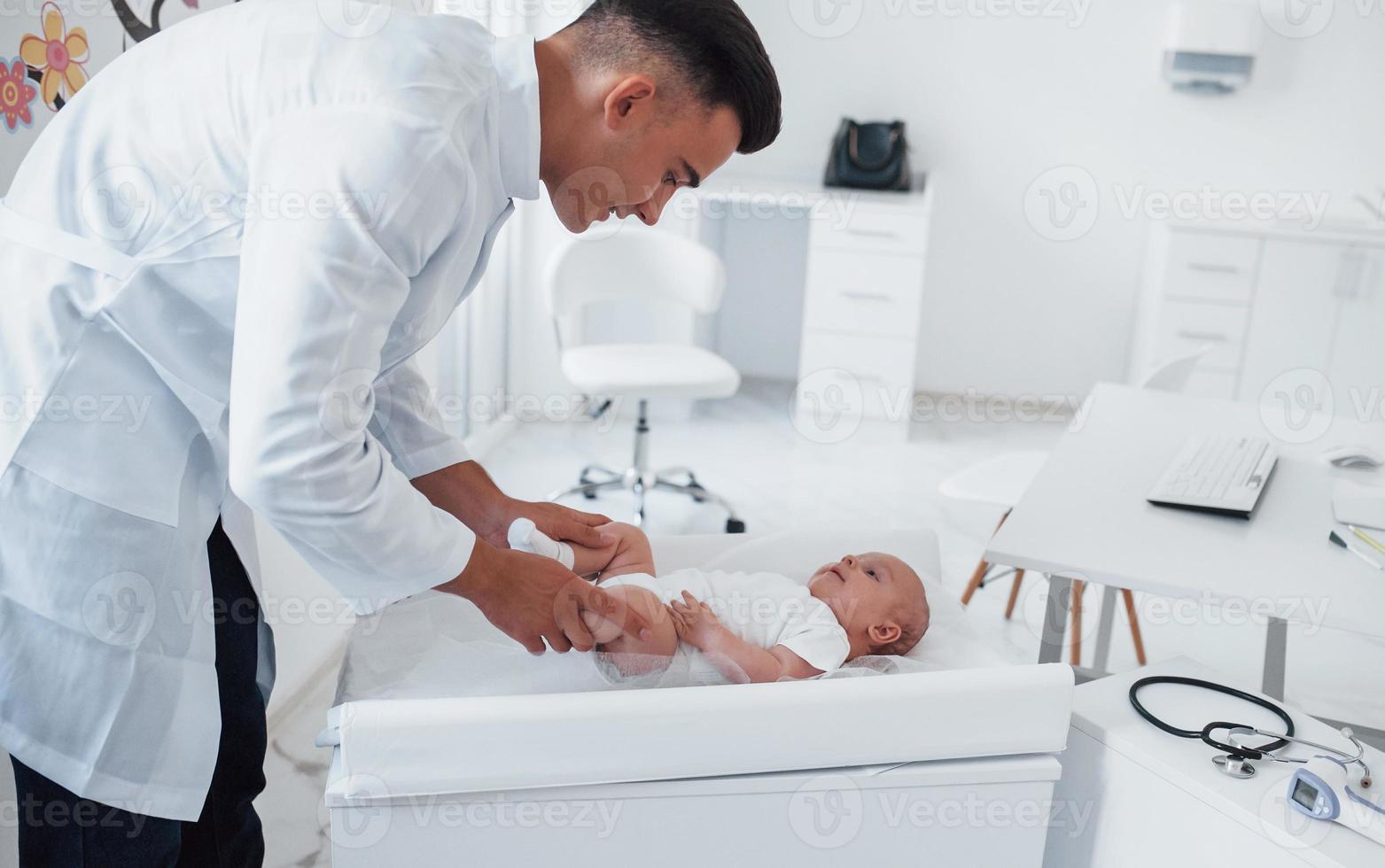 Young pediatrician is with little baby in the clinic at daytime photo
