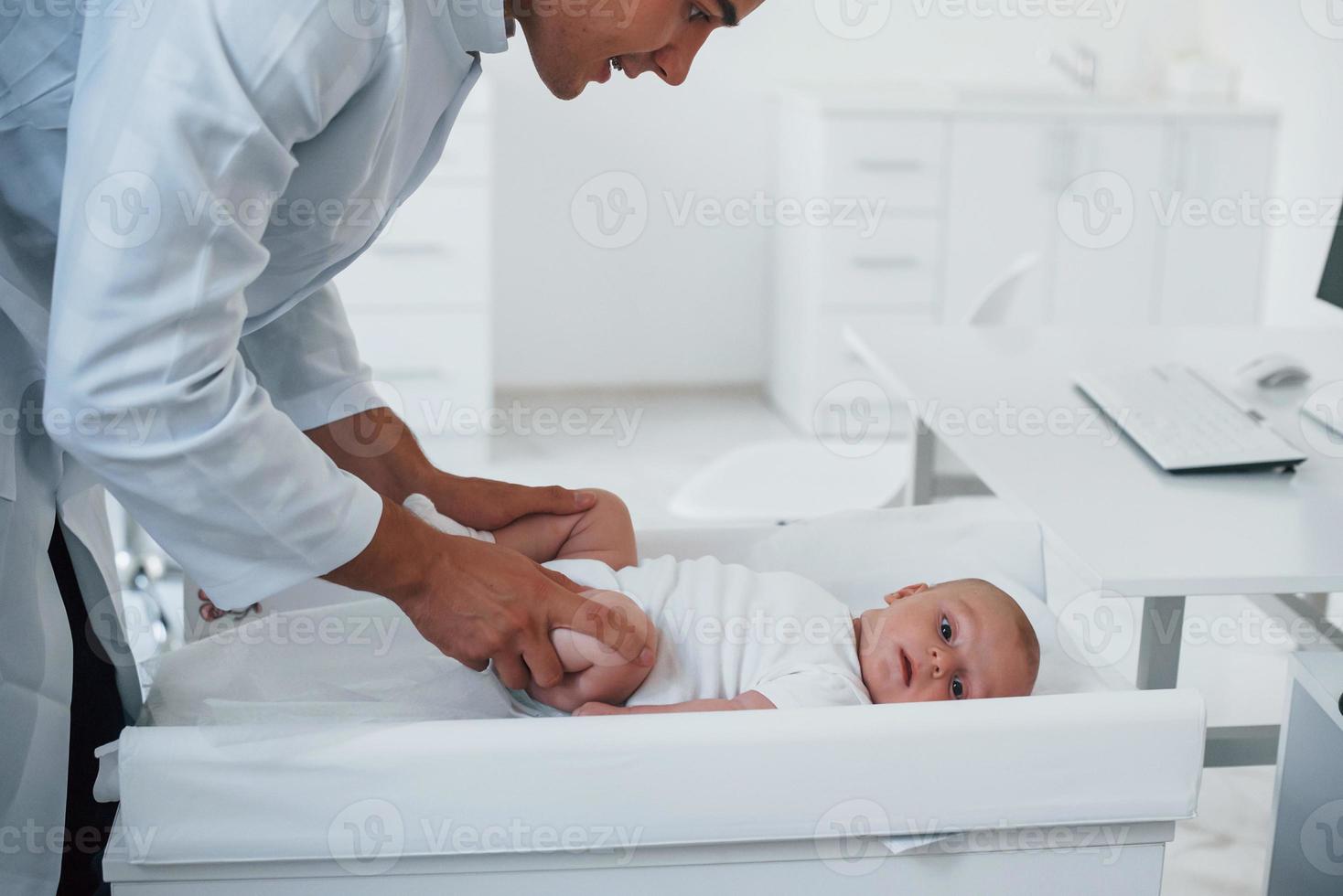 Young pediatrician is with little baby in the clinic at daytime photo