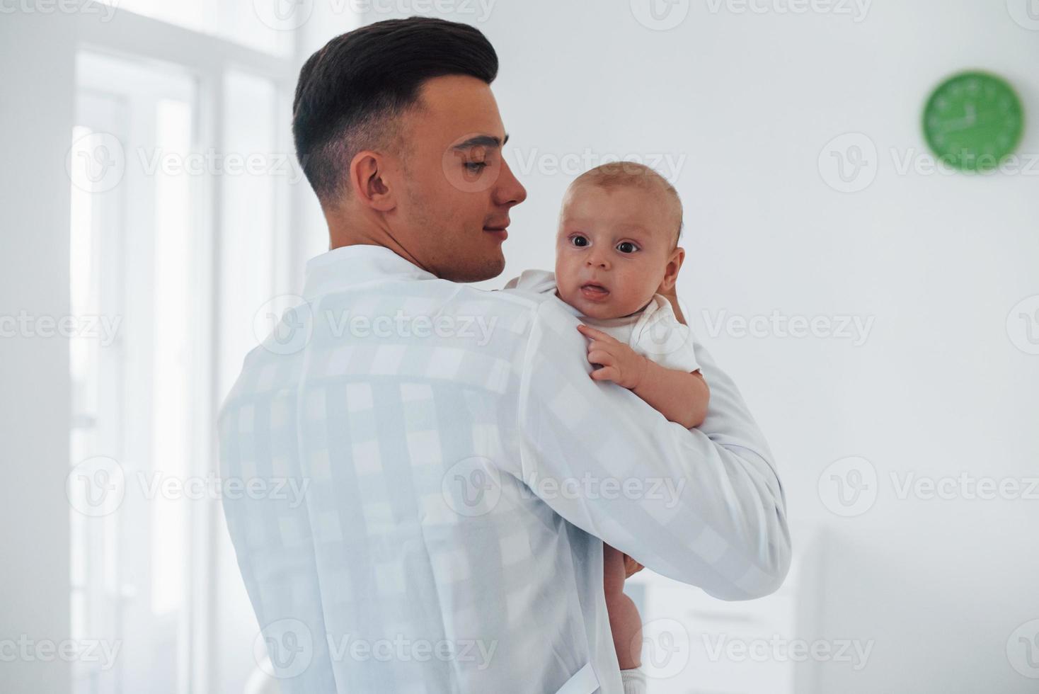 Stands and holds baby on the hands. Young pediatrician is in the clinic at daytime photo
