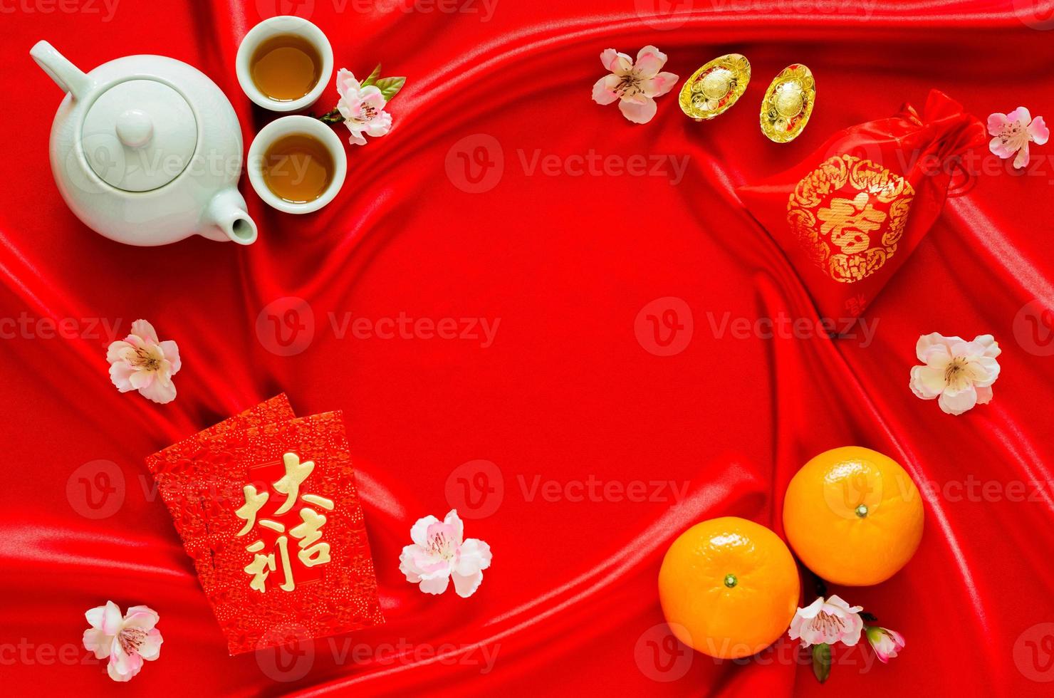 Red satin cloth background with tea set, ingots, red bag word means wealth, oranges and red envelope packets or ang bao word means auspice for Chinese new year concept. photo