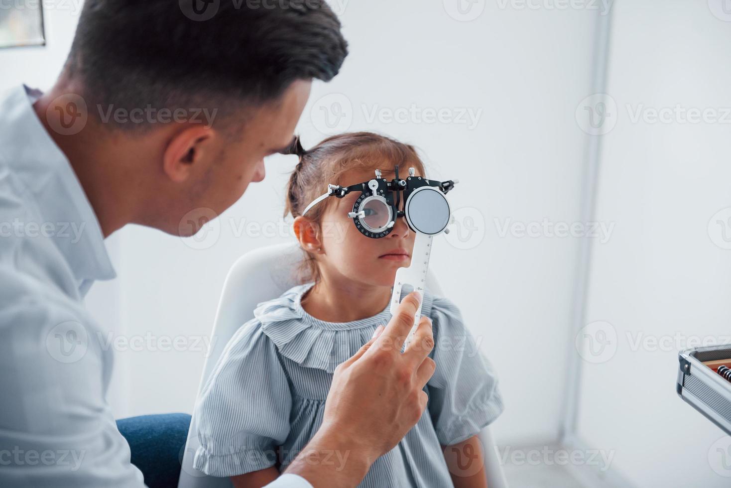 probando la visión. joven oftalmólogo está con una pequeña visitante en la clínica foto