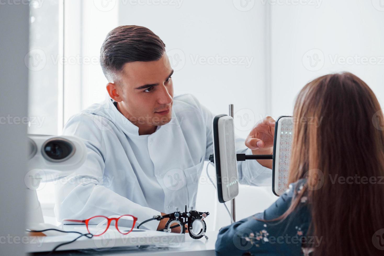 dos paneles sobre la mesa. joven oftalmólogo está con una pequeña visitante en la clínica foto