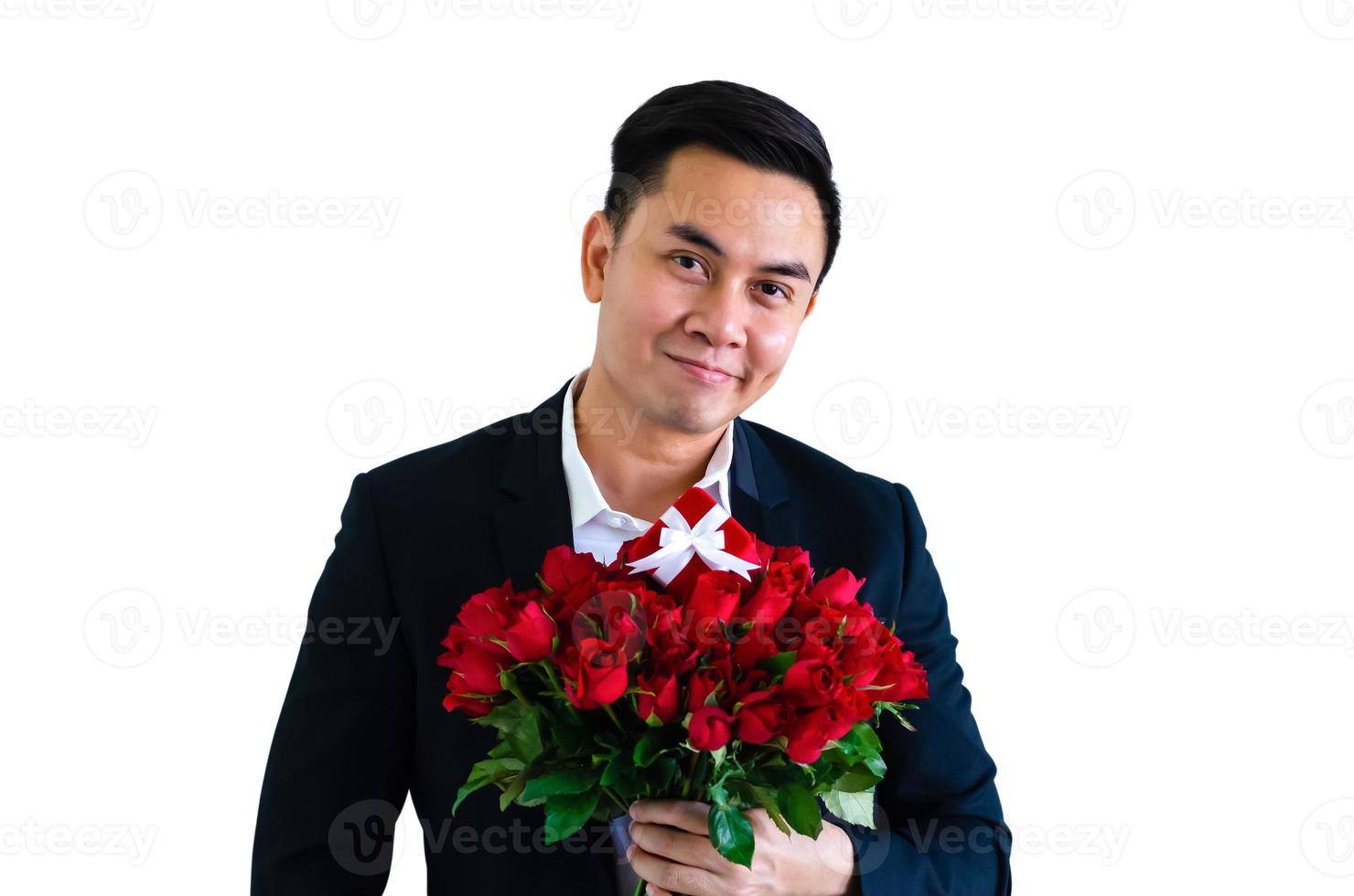 Asian man wearing black suit holding a bouquet of red roses and red gift box isolated in white background for anniversary or Valentine day concept. photo