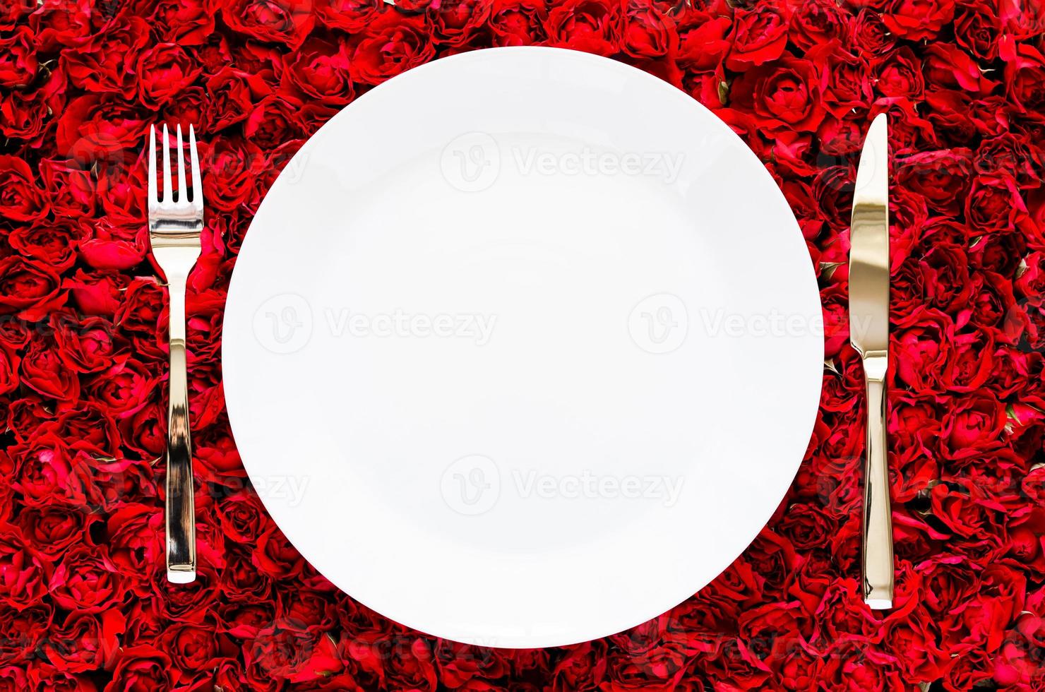 White plate with knife and fork on red rose background for dining, anniversary and Valentine day concept. photo