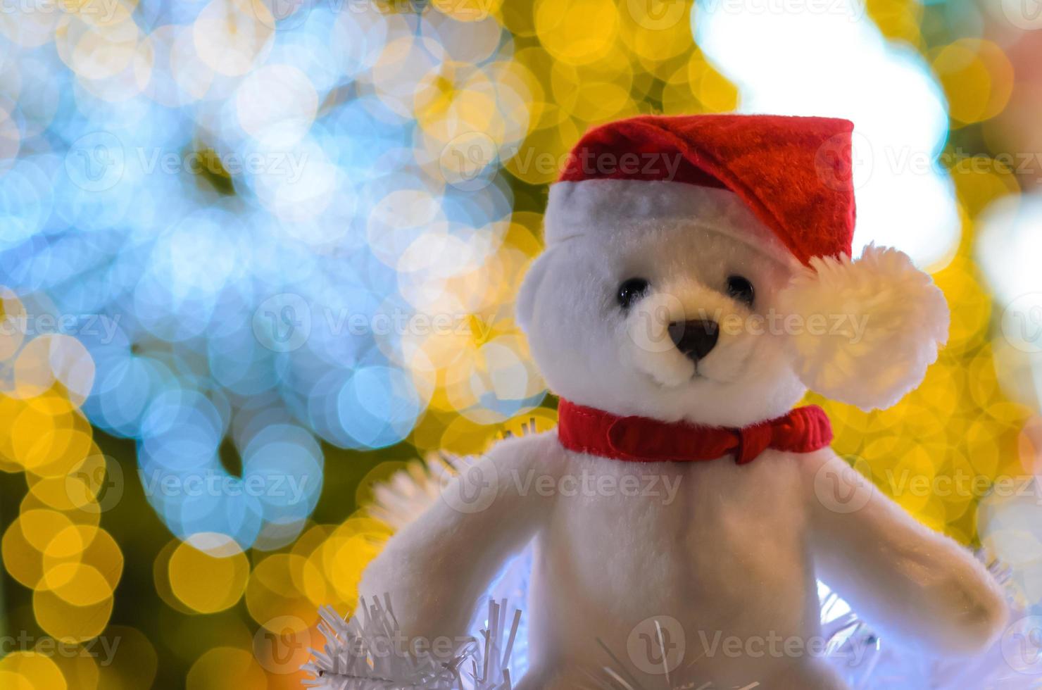 Selective focus on Santa claus teddy bear eyes who wearing hat sitting in front of colorful bokeh lights of Christmas tree. photo