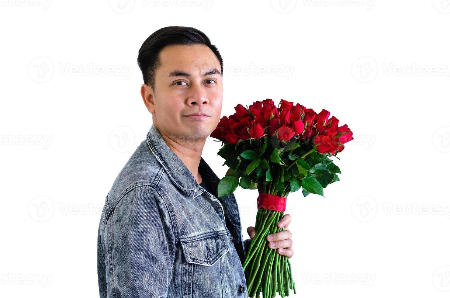 hombre asiático con chaqueta de jeans sosteniendo un ramo de rosas rojas aisladas en fondo blanco para el concepto de aniversario o día de san valentín. foto