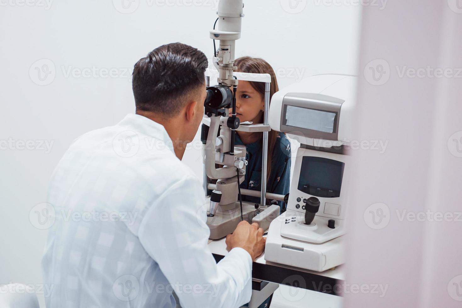 Young ophthalmologist is with little female visitor in the clinic photo